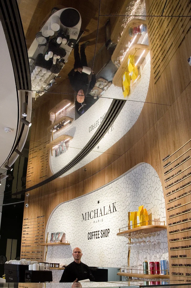 Intérieur élégant d'un coffee shop nommé Michalak, avec barista derrière le comptoir et décorations murales en bois et métal.
