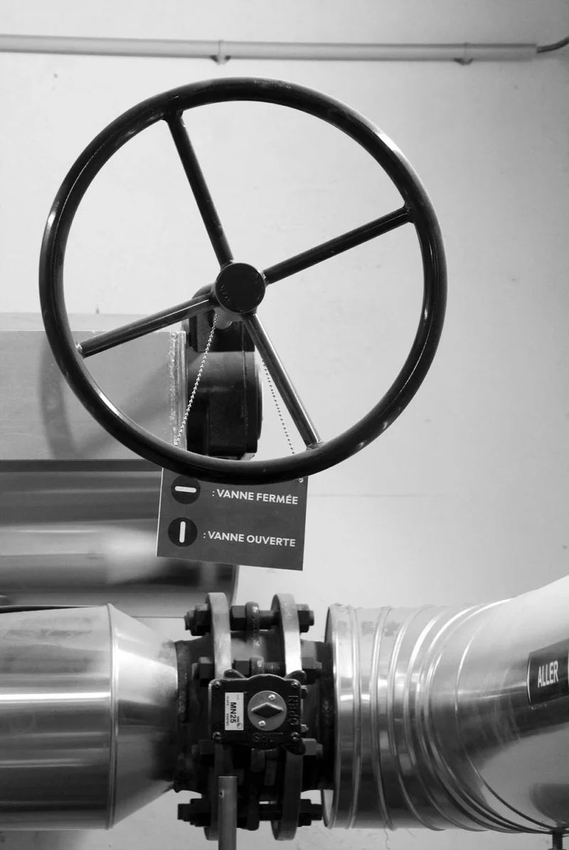 Vanne industrielle fermée avec un volant de commande et une plaque signalétique indiquant les positions ouverte et fermée
