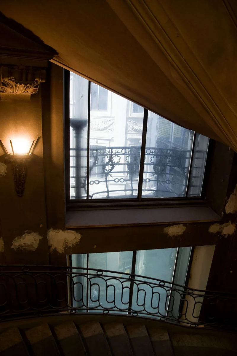 Balcon en fer forgé devant une fenêtre éclairée dans un bâtiment ancien, vue depuis un escalier en colimaçon sombre