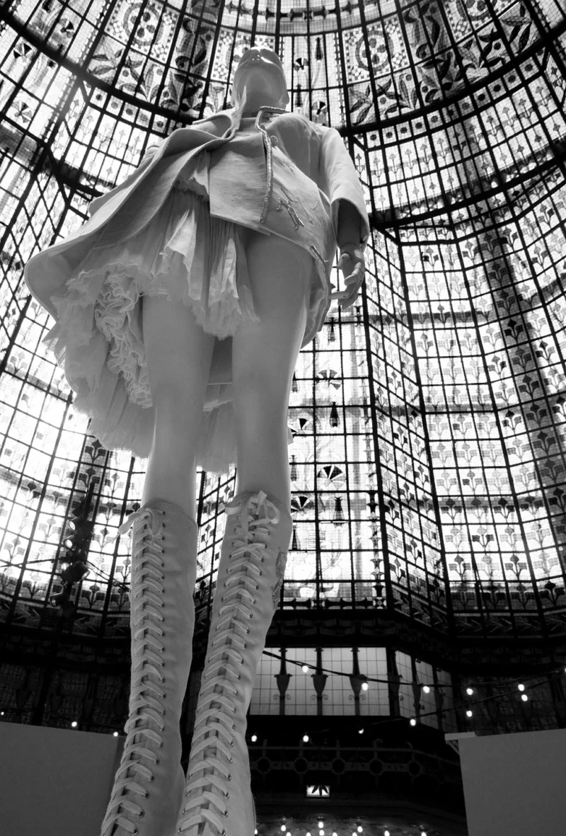 Mannequin vêtu d'une robe volumineuse à structure osseuse visible, sous une verrière ornée de motifs géométriques