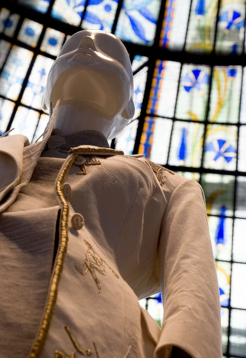 Mannequin vêtu d'un uniforme historique avec casque transparent, exposé devant une vitrine colorée à motifs géométriques