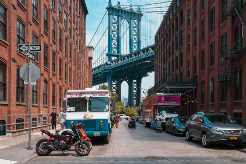 Thierry · 14/06/2024 · 3840 x 2560 Rue étroite en ville avec un camion à glace cream, des voitures, un deux-roues et le pont de Brooklyn en arrière-plan