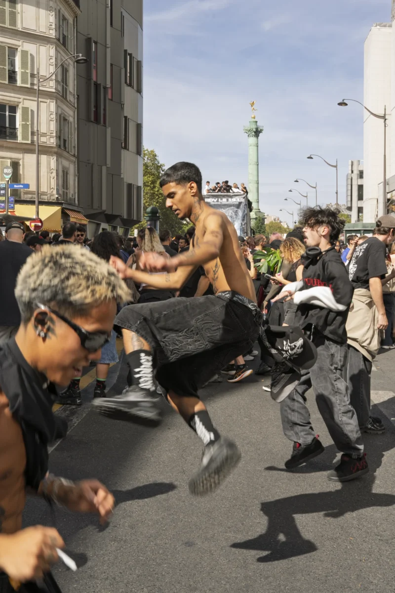Thierry · 19/09/2026 · 2560 x 3840 Groupe de personnes en mouvement dans une rue animée devant un monument emblématique, ambiance festive et énergique