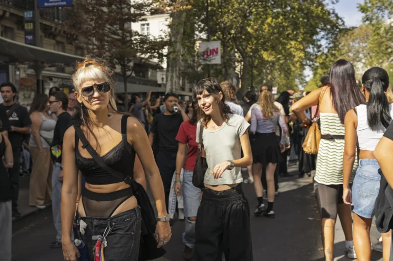 Thierry · 19/09/2026 · 3840 x 2560 Deux femmes marchant main dans la main dans une rue animée entourées d'une foule en mouvement sous un ciel dégagé