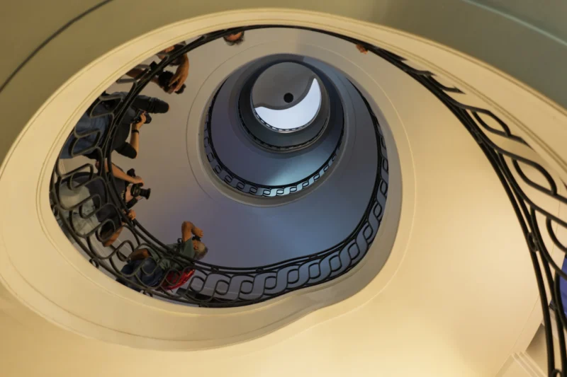 Vue plongeante d'un escalier en colimaçon avec des personnes en mouvement, éclairé par une lumière douce et uniforme