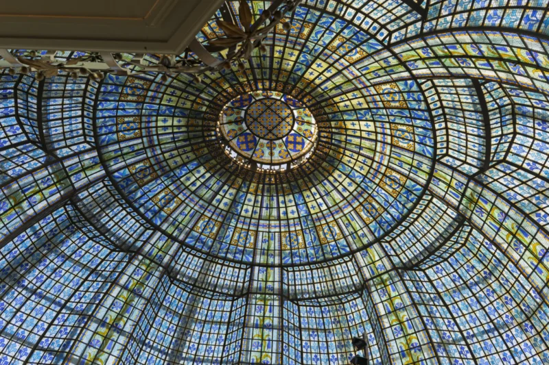 Vue plongeante d'une coupole vitrée aux motifs géométriques colorés et lumineux, inspirant une sensation d'infini
