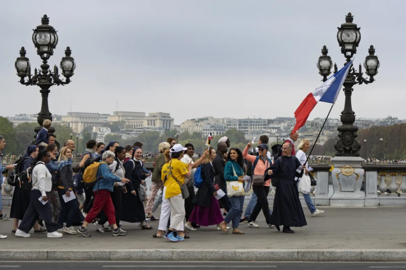 Thierry · 26/09/2026 · 3840 x 2560 Groupe de personnes marchant sur un pont parisien avec une personne brandissant un drapeau français, ambiance touristique