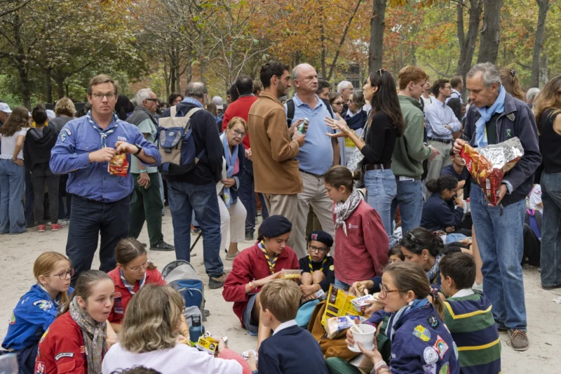 Thierry · 26/09/2026 · 3840 x 2560 Groupe de personnes assises et debout dans un parc, partageant un repas en plein air avec des emballages alimentaires.