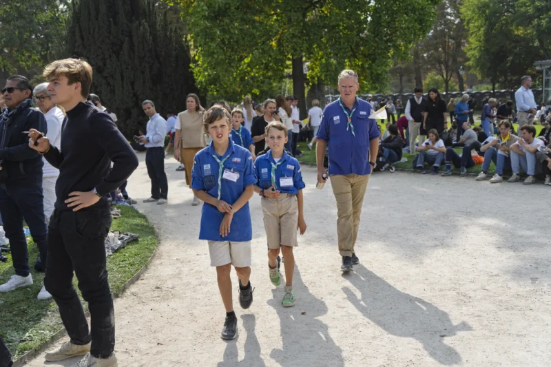 Thierry · 26/09/2026 · 3840 x 2560 Trois jeunes participants en tenue bleue de scoutisme marchent en plein air sous l'accompagnement d'un adulte, devant