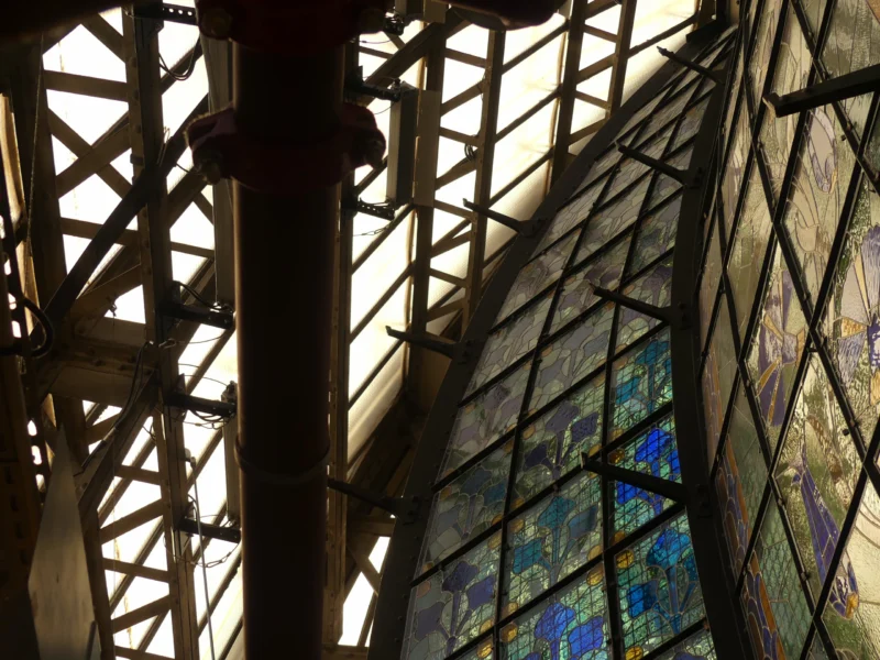 Structure métallique et vitraux colorés formant une verrière lumineuse avec des motifs artistiques et des jeux de lumière
