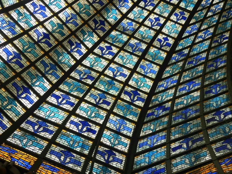 Voute intérieure composée de vitraux colorés représentant des motifs floraux bleus et blancs, formant un réseau géométrique