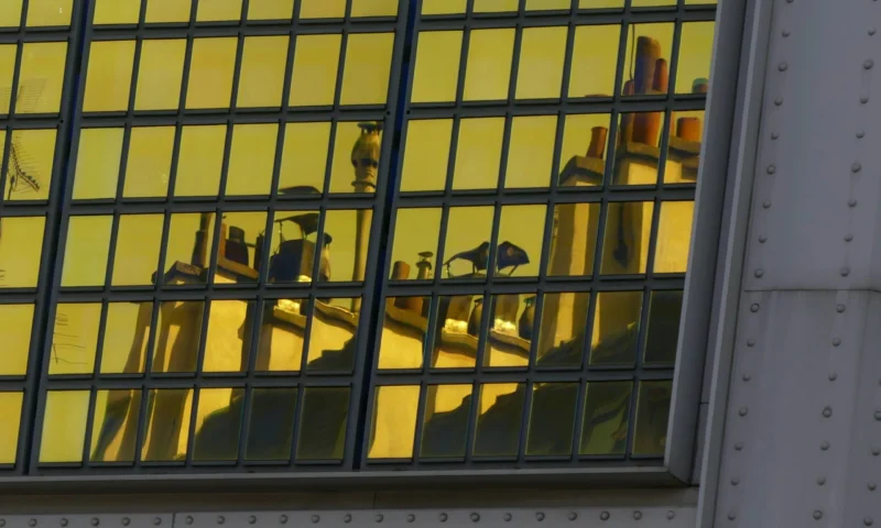 Reflet d'un intérieur lumineux avec des bouteilles et des objets dans une vitrine à barreaux jaunes, vue depuis l'extérieur.