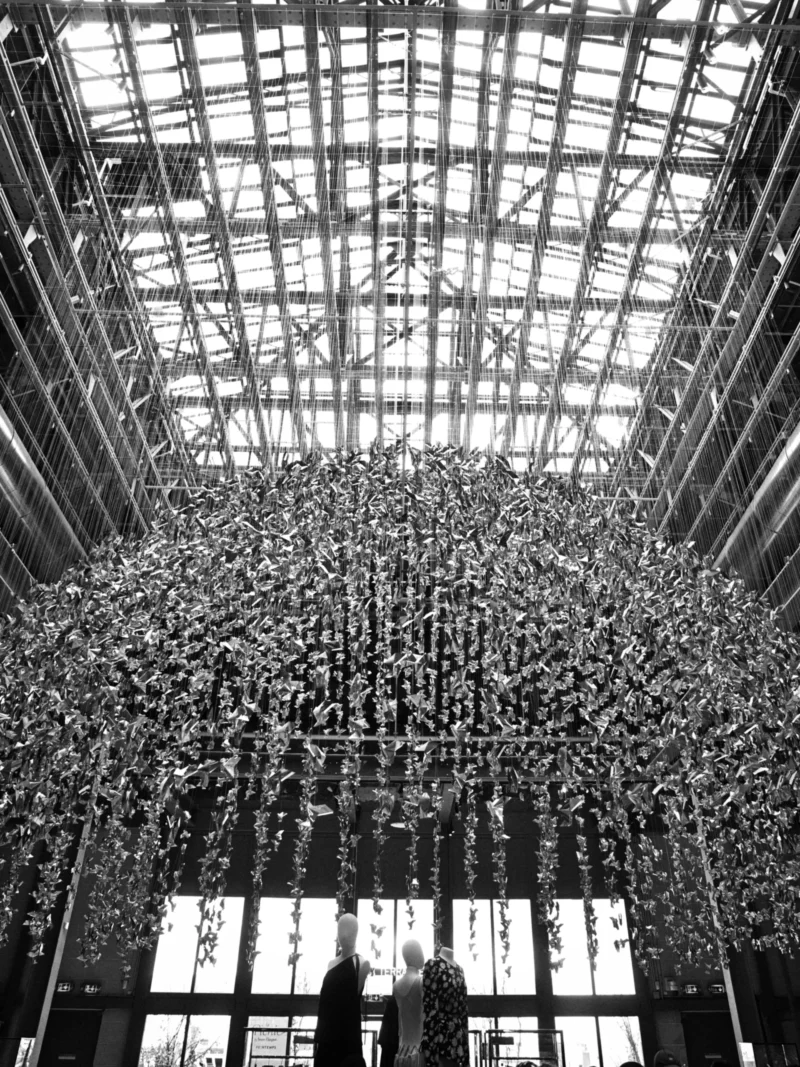 Installation artistique suspendue représentant une multitude d'oiseaux en vol à l'intérieur d'une structure architecturale