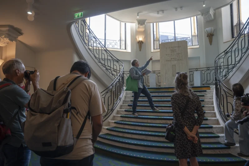 Un guide explique quelque chose à un groupe de visiteurs dans un escalier élégant avec une inscription sur un mur et