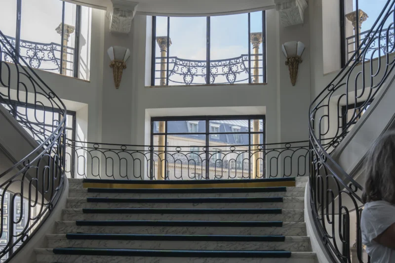Escalier intérieur élégant avec balustrades en fer forgé, deux volées symétriques et murs clairs, vue vers un étage