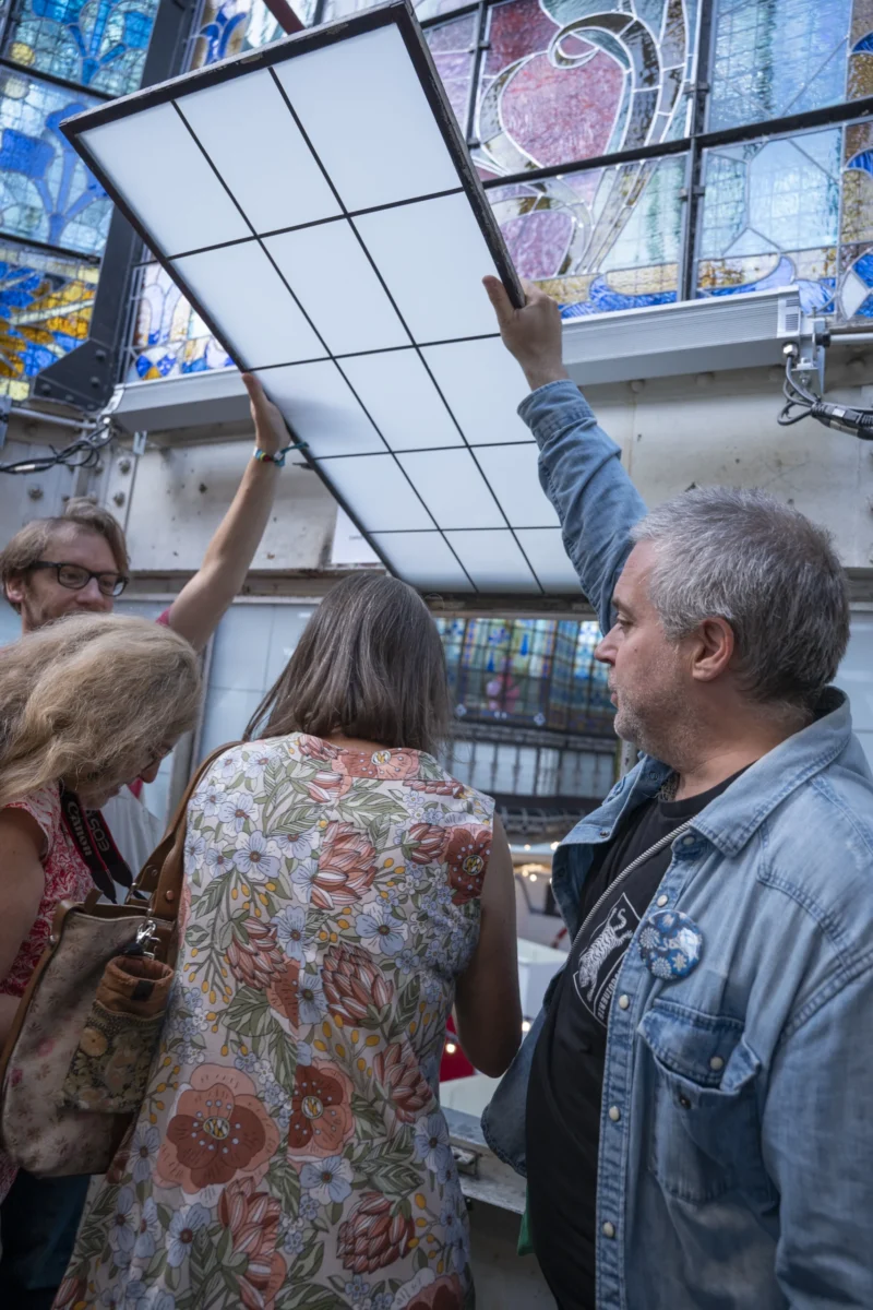 Un groupe de personnes observe une grande vitrine colorée avec des motifs artistiques, un homme pointant du doigt vers