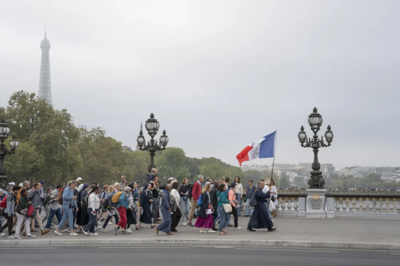Alice · 26/09/2026 · 3840 x 2560 Groupe de personnes marchant sur un pont parisien avec un drapeau français, Eiffel Tower en arrière-plan sous un ciel couvert