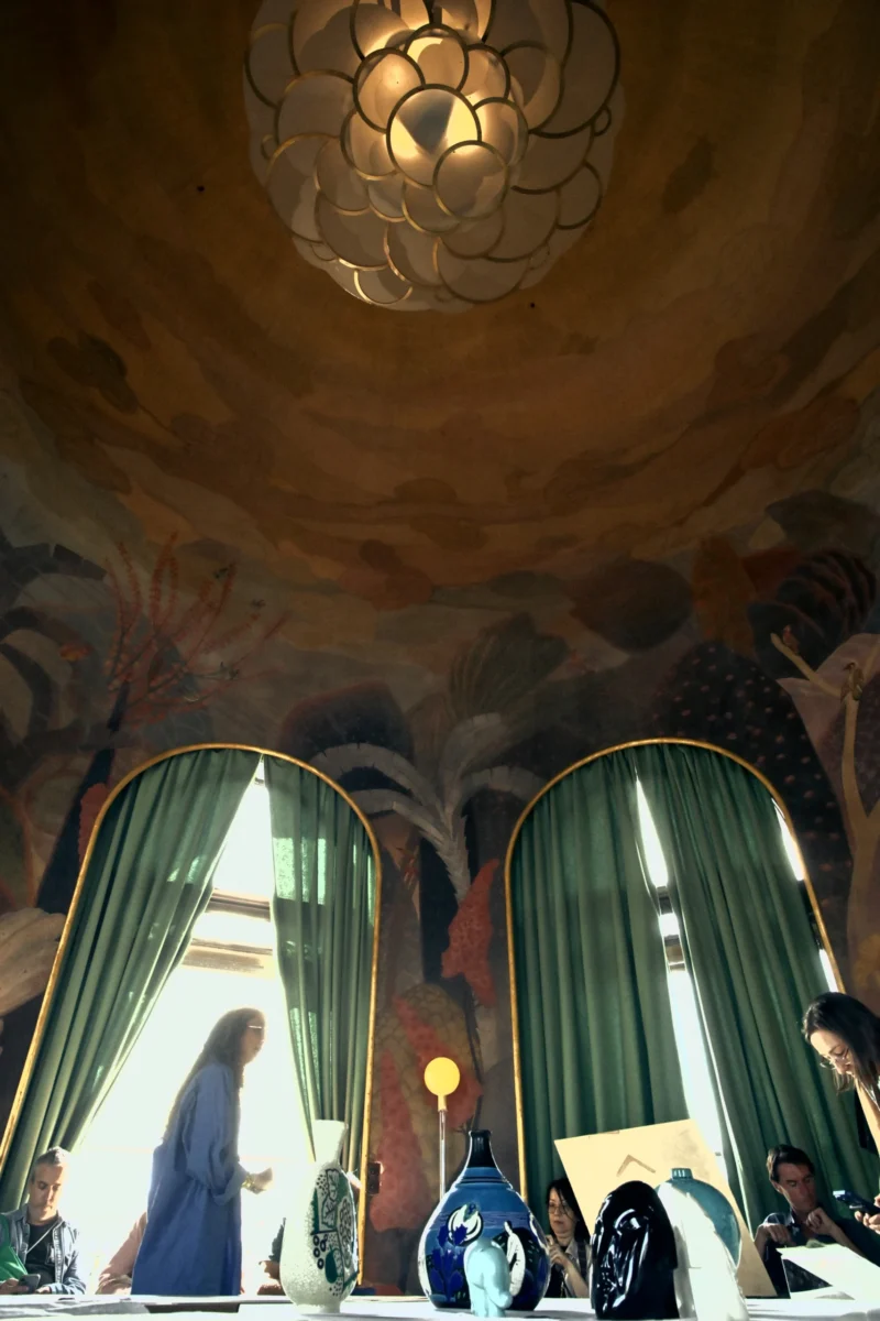 Salle élégante avec lustre doré et tentures vertes, des personnes assises autour d'une table décorée d'objets artisanaux