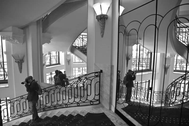 Escalier élégant avec balustrades ornées et personnes photographiant l'architecture intérieure d'un bâtiment historique