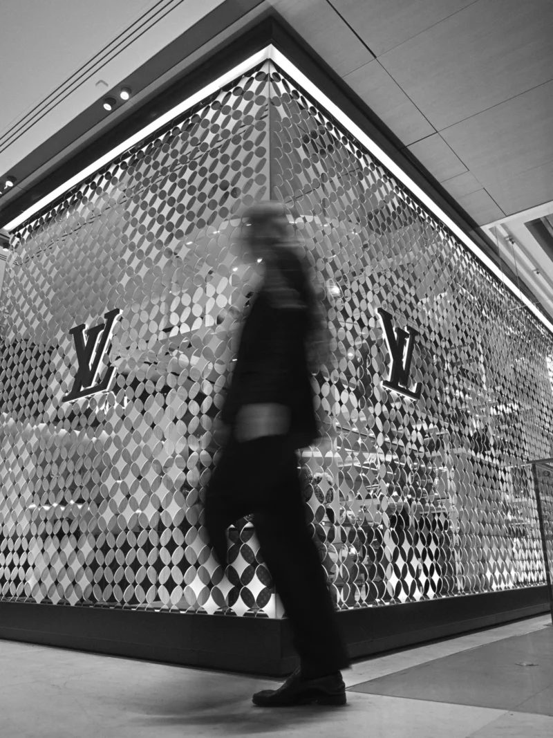 Personne marchant devant une façade décorée de motifs géométriques métalliques reflétant des logos stylisés, en intérieur