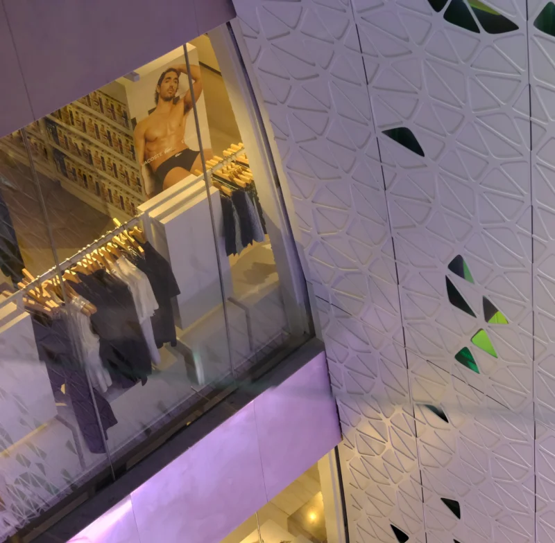 Vitrine lumineuse d'un magasin de vêtements avec mannequin et vêtements exposés, reflétée dans un miroir, ambiance moderne