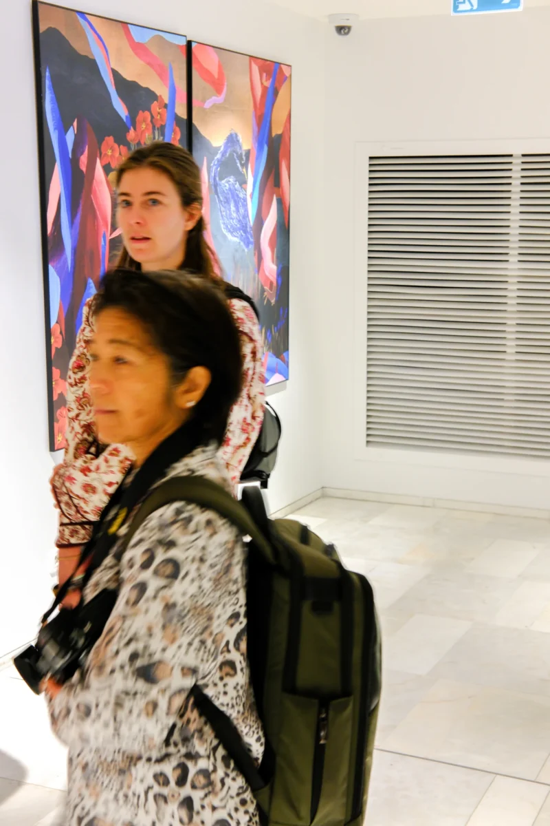 Deux personnes observent une peinture colorée dans un espace intérieur lumineux, l'une avec un appareil photo autour du cou.
