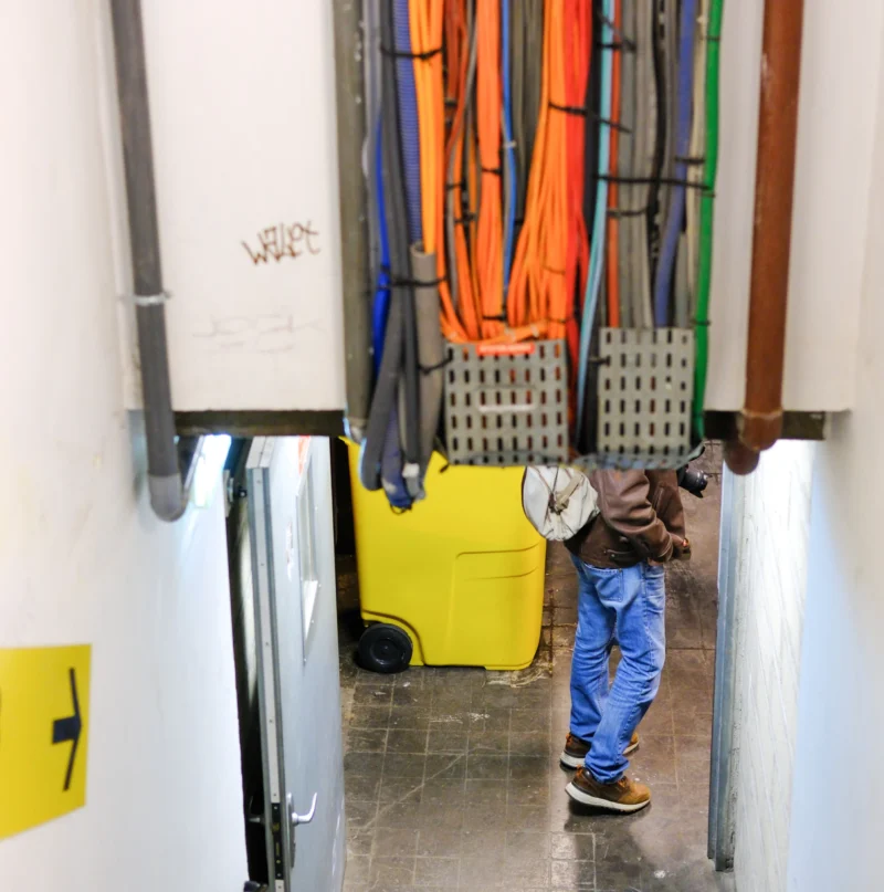Un individu en tenue de travail transporte un sac dans un espace industriel rempli de câbles colorés suspendus et