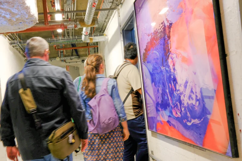 Trois personnes observent une grande peinture abstraite aux tons bleus et rouges dans un espace intérieur éclairé
