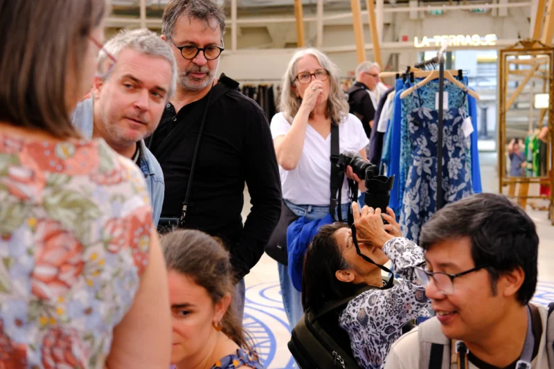 Groupe de personnes en discussion dans un espace d'exposition textile, certains prenant des photos avec des appareils