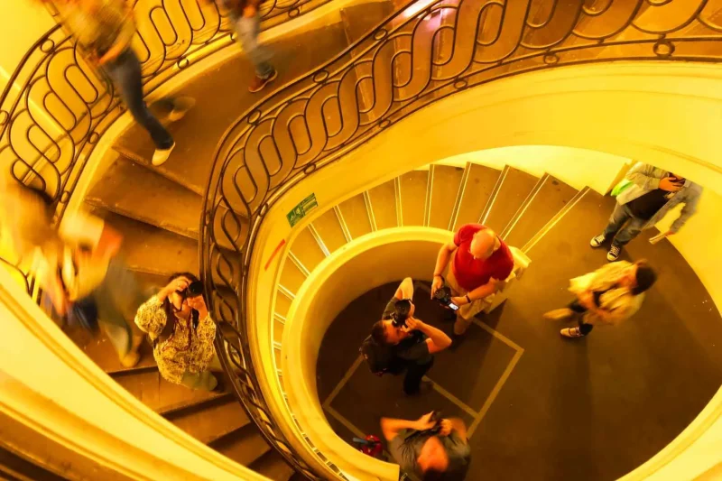 Vue aérienne d’un escalier en colimaçon orné où des personnes montent et descendent dans un bâtiment lumineux et élégant