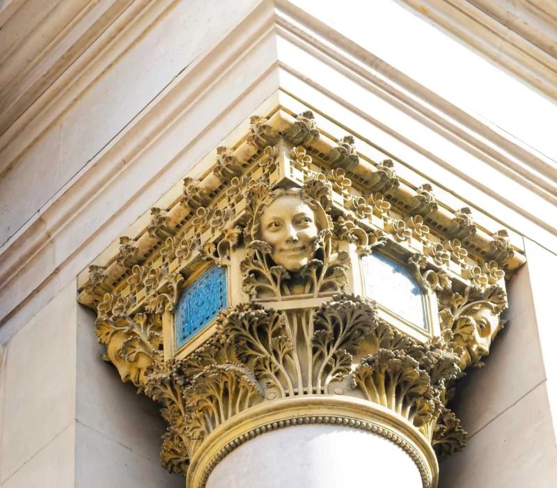 Détail architectural doré représentant une tête souriante encadrée par des motifs végétaux et une fenêtre en arc brisé