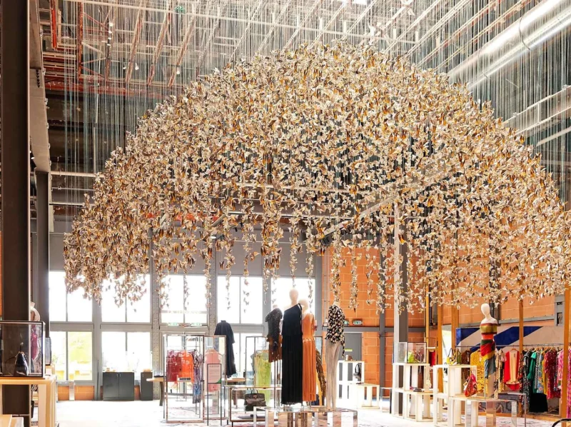 Arbre décoratif suspendu au plafond dans un magasin de vêtements, entouré de mannequins et d’étals colorés sous une lumière