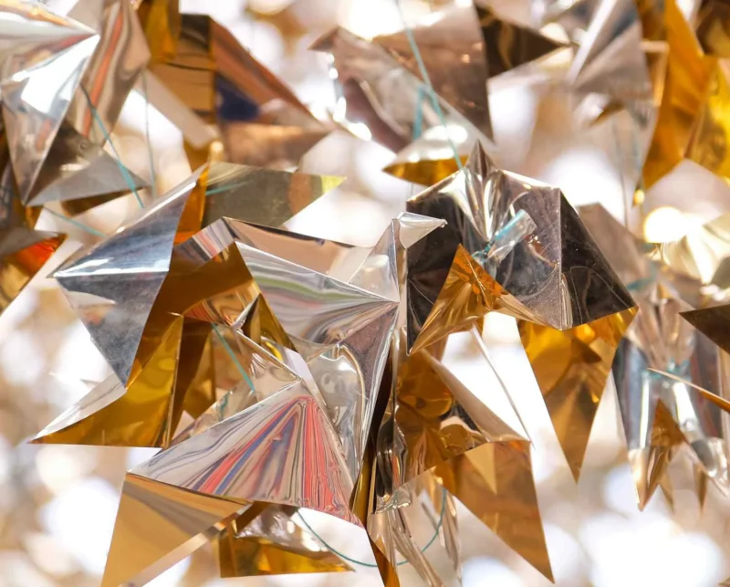 Assemblage de triangles en papier métallisé aux reflets dorés et multicolores, disposés en volume pour former une structure