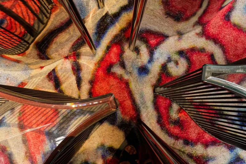 Vue plongeante d'un sol décoratif aux motifs colorés et de sièges métalliques en forme de vagues dans un espace public.