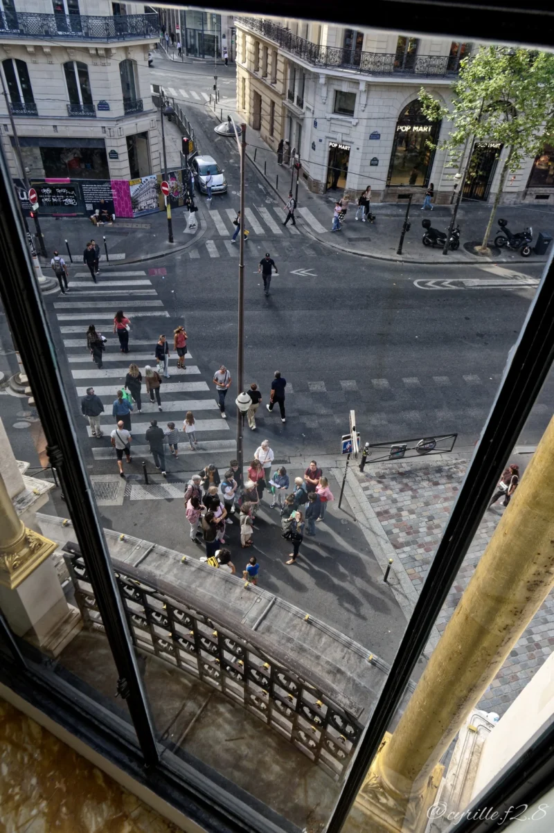 Vue depuis un bâtiment sur une intersection animée avec piétons, véhicules et bâtiments typiques d'une ville européenne