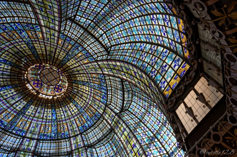 Vue intérieure d'une coupole vitrée aux motifs colorés et géométriques, illuminée par la lumière naturelle, avec