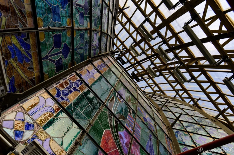 Vue intérieure d’une structure architecturale en verre coloré et métal formant un motif géométrique complexe, vue vers