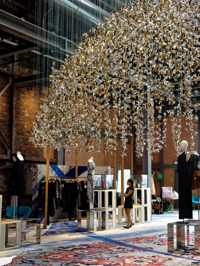 Installation artistique intérieure représentant des arbres métalliques suspendus dans un espace d'exposition avec