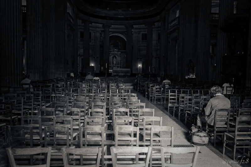 Cyrille · 26/09/2026 · 2026 x 1347 Intérieur d’une église vide avec des rangées de bancs et quelques personnes assises dans la pénombre, ambiance calme