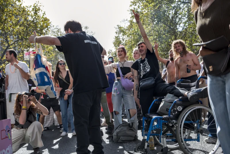 Frédéric · 19/09/2026 · 2517 x 1680 Groupe de personnes en manifestation en extérieur, certaines levées, d'autres assises en fauteuil roulant, ambiance festive
