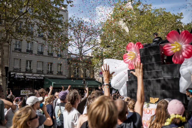 Frédéric · 19/09/2026 · 2517 x 1680 Foule en liesse sous des confettis, acclamant un véhicule décoré de fleurs géantes lors d'une parade festive en ville.