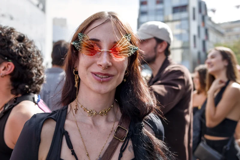 Frédéric · 19/09/2026 · 2517 x 1680 Femme souriante en accessoires colorés participant à une manifestation ou rassemblement en extérieur, avec des lunettes