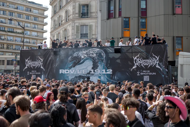 Frédéric · 19/09/2026 · 2498 x 1680 Foule dense assistant à un événement public avec une grande bannière promotionnelle pour un spectacle ou jeu vidéo devant