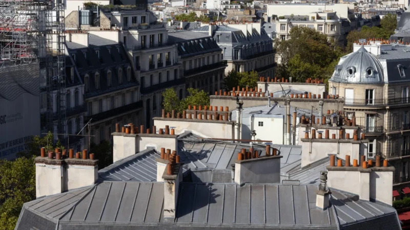 Vue aérienne de toits parisiens typiques avec cheminées en terre cuite et antennes, sous un ciel dégagé et ensoleillé