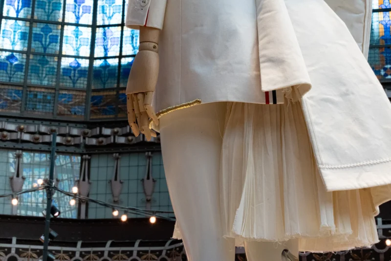 Mannequin mécanique vêtu d'une robe blanche à jupe volumineuse et veste assortie, dans un espace vitré coloré avec