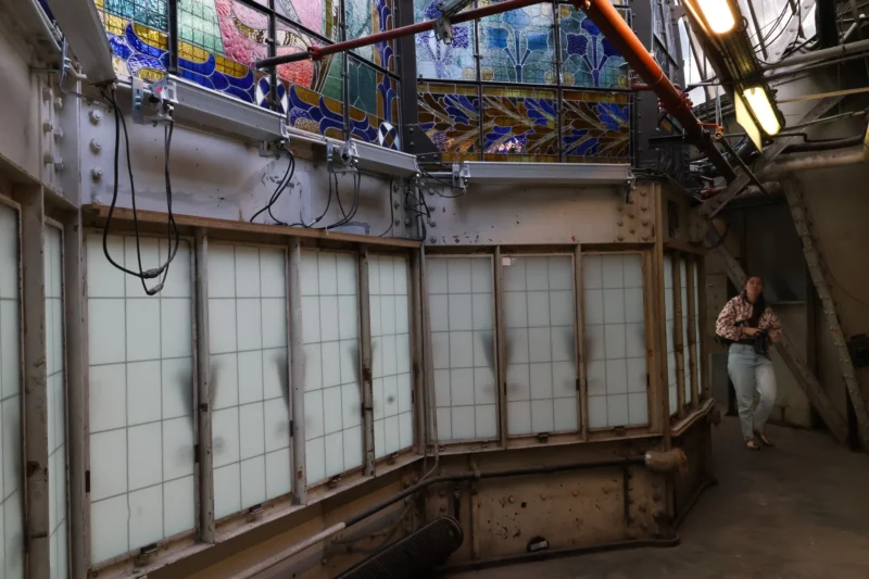 Intérieur d’un wagonnet ancien avec vitraux colorés et une personne marchant dans un espace industriel partiellement éclairé
