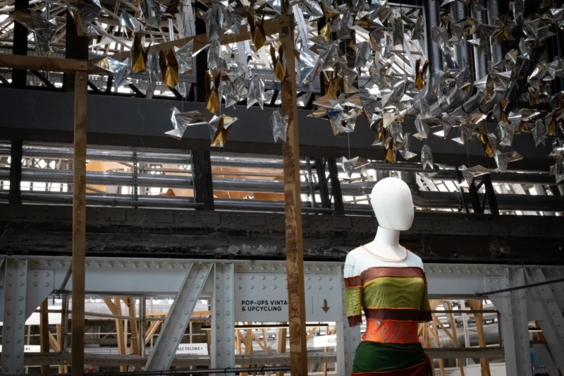 Mannequin vêtu d'une robe colorée dans un espace industriel suspendu sous une installation artistique de formes métalliques