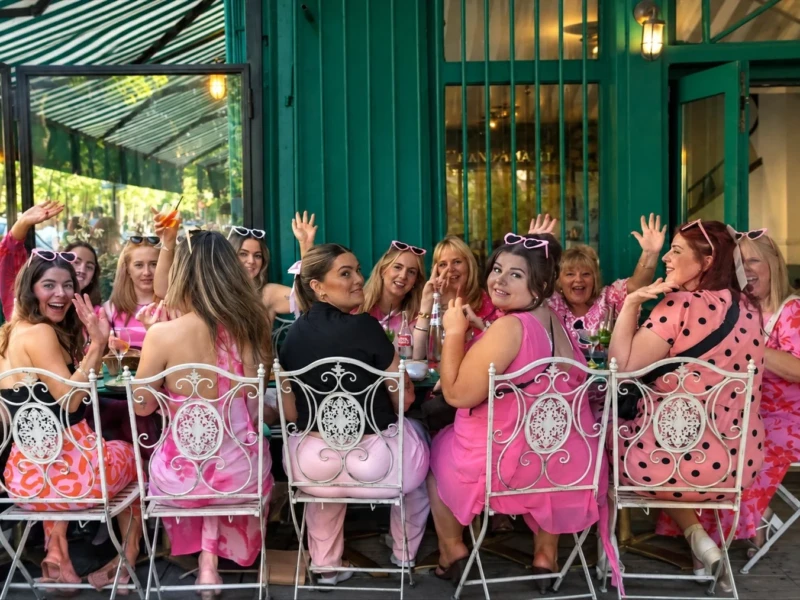 Bao · 12/09/2026 · 1497 x 1014 Cette photographie montre un groupe de femmes célébrant un événement, probablement une fête thématique. Le sujet principal est ce groupe joyeux, assis sur des chaises roses à motifs, vêtues de tenues festives (pantalons et chapeaux assortis).La composition est dynamique, avec un cadrage serré sur les participantes, créant une ambiance conviviale. La lumière est naturelle et douce, probablement prise en extérieur. Les couleurs dominantes sont le rose vif, le vert (pour le fond) et des touches de noir et blanc.Le style est décontracté et festif, évoquant une ambiance joyeuse et amicale.