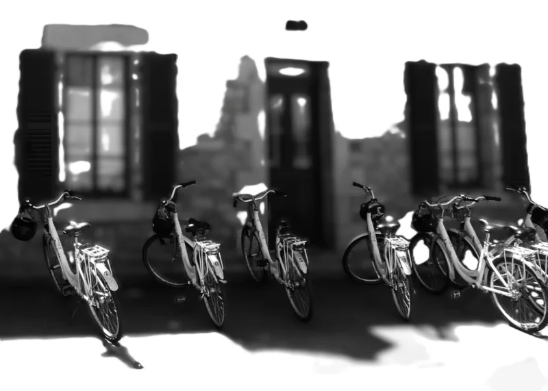 Cécile · 16/07/2021 · 2249 x 1606 Six vélos alignés devant des bâtiments urbains en noir et blanc, créant une silhouette contrastée avec des ombres marquées