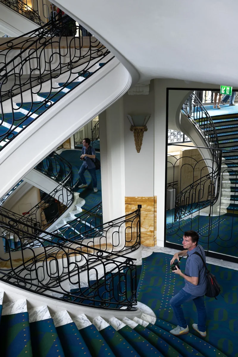 Escalier élégant avec balustrades en fer forgé et deux personnes descendant ou prenant des photos dans un bâtiment